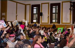 Audience with signage in protest of the proposed co-location