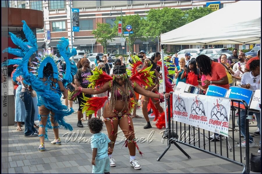 Children enjoy dancing with Sesame Flyers’ costumed masqueraders to the sounds of Eruption Steel Orchestra