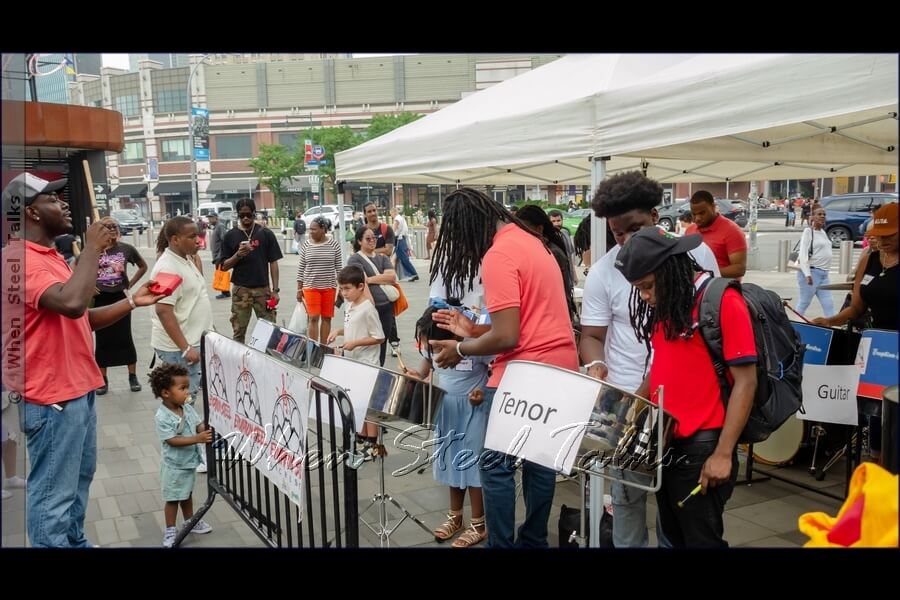 After several minutes in basics, it’s time for the steelpan ‘newbies’ to sound out their first tune, with tutors by their sides, clapping out the beat, while another in front keeps time on the cow bell